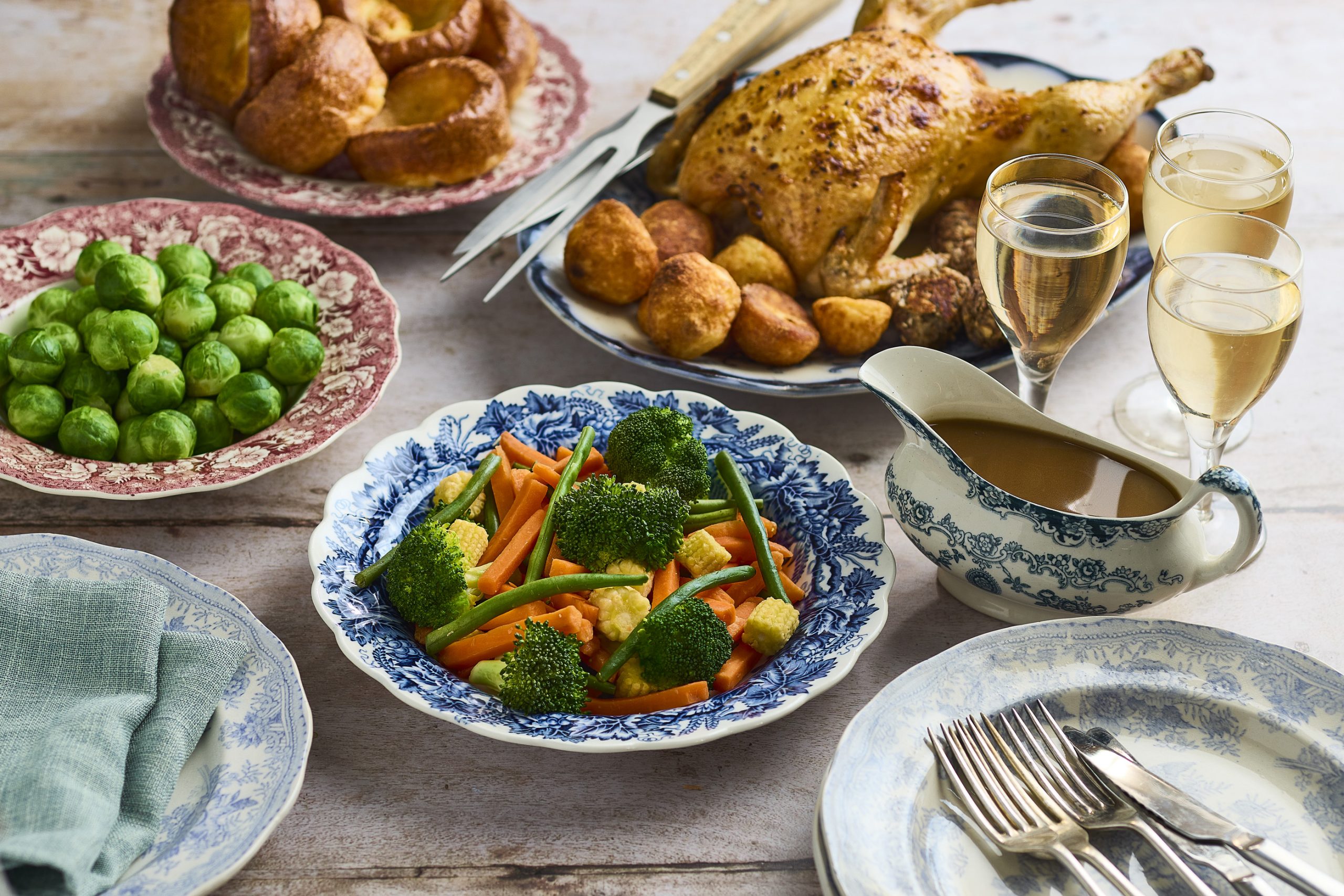 A bowl of mixed veg, surrounded by the other pieces of a roast dinner on separate plates