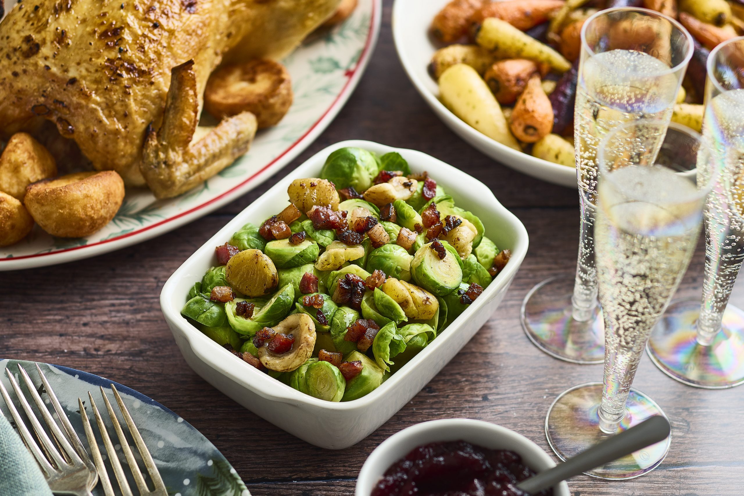 A bowl of sprouts, surrounded by the other pieces of a roast dinner on separate plates